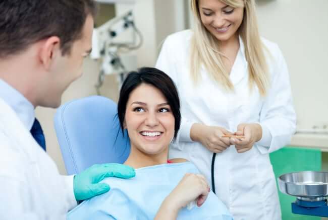 woman sitting in dental chair talking to dentist and assistant