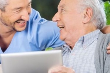 male dentist smiling as his elderly male patient looks at his new smile