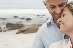 middle-aged couple smiling and leaning in to each other on a beach